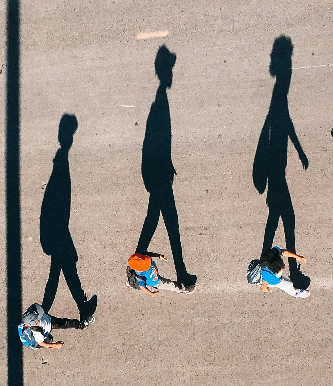 three people walking with enlarged shadows from above